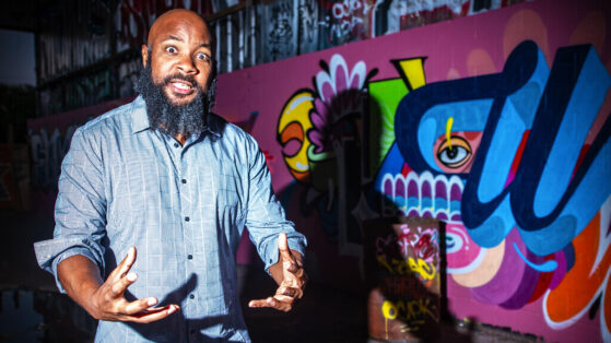 JClay is asking you why in front of an urban graffiti wall
