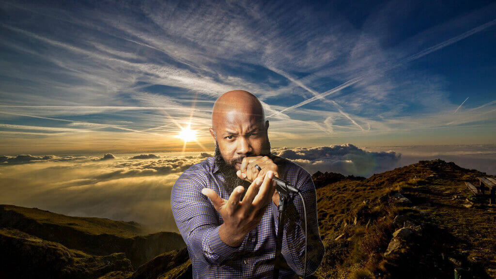 JClay holding a microphone in front of a mountain