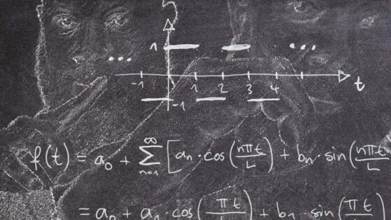 Spiritual Math Secrets and The Divine Equation JClay on the chalkboard holding up a 1 and a 0 with math equations