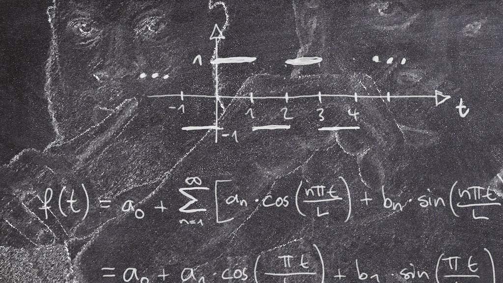 JClay on the chalkboard holding up a 1 and a 0 with math equations
